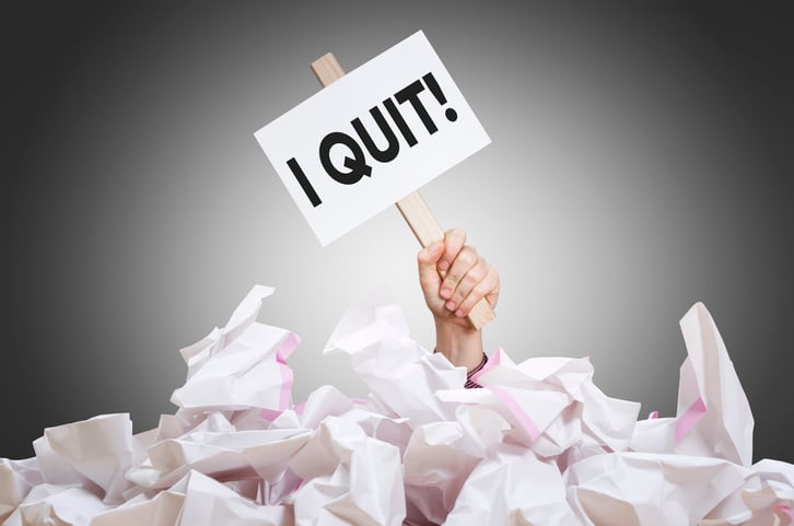 a man buried in paper holding an I Quit sign